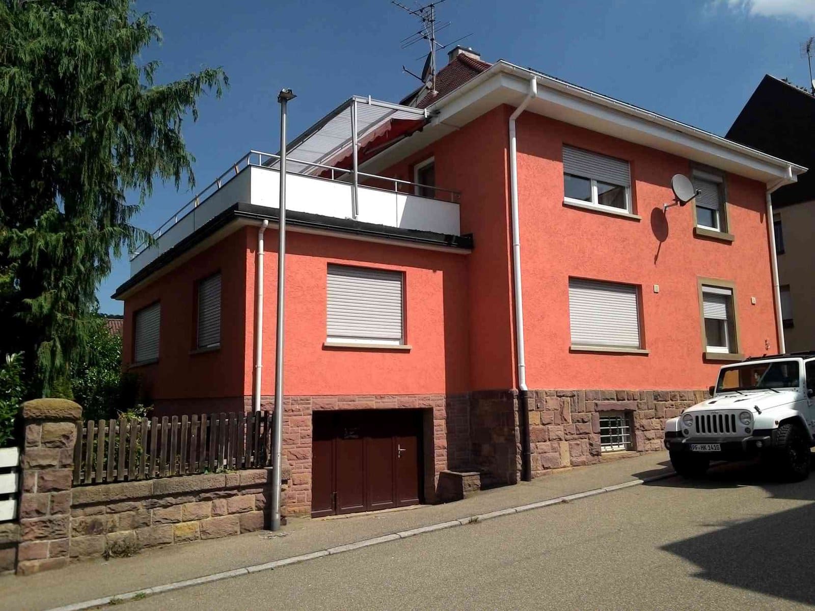 Fassadensanierung mit roter Putzschicht und Steinbasis an einem Mehrfamilienhaus.