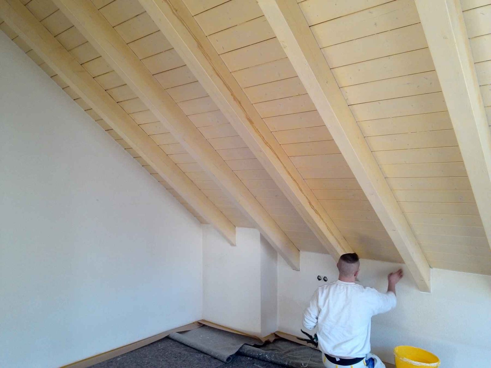 Maler trägt Holzverkleidung an Dachschräge auf.